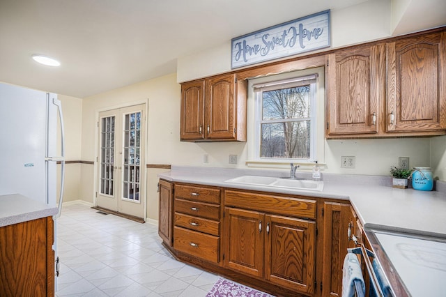 kitchen featuring light countertops, brown cabinetry, baseboards, and a sink