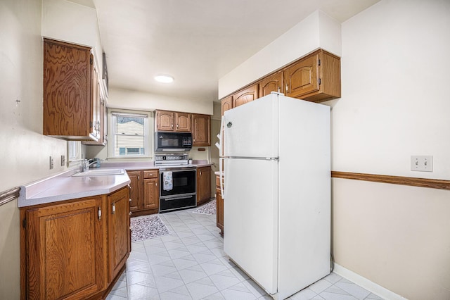 kitchen featuring black microwave, freestanding refrigerator, electric stove, brown cabinetry, and a sink