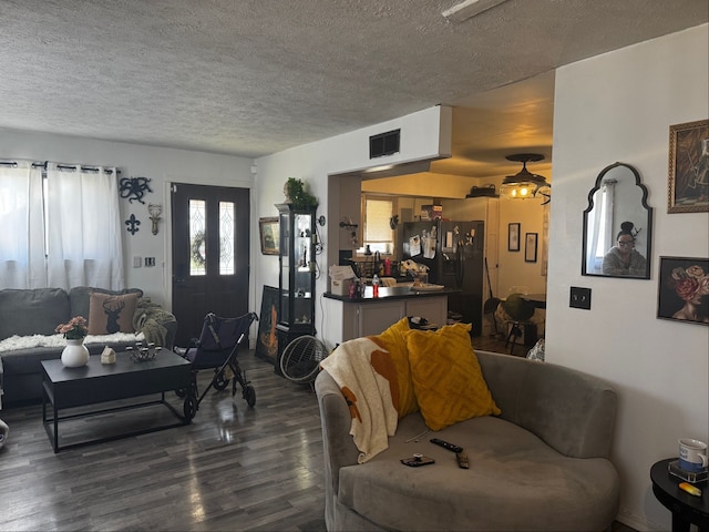 living room featuring visible vents, a textured ceiling, and dark wood finished floors