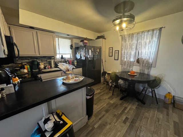 kitchen with dark countertops, tasteful backsplash, dark wood finished floors, a peninsula, and black refrigerator with ice dispenser