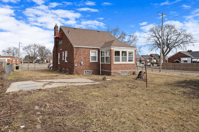 rear view of house with fence, a shingled roof, a chimney, a lawn, and brick siding