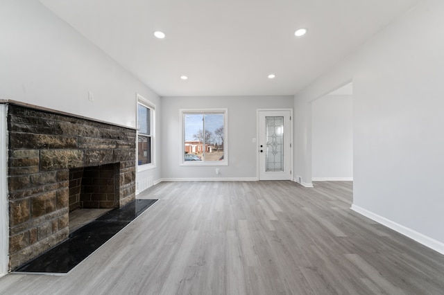 unfurnished living room with a stone fireplace, recessed lighting, wood finished floors, and baseboards