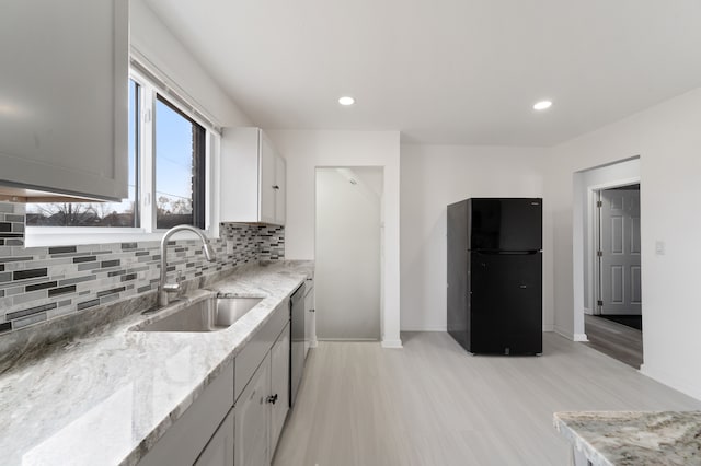 kitchen featuring baseboards, freestanding refrigerator, a sink, stainless steel dishwasher, and backsplash