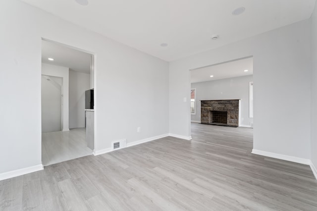 unfurnished living room with visible vents, baseboards, light wood-style floors, and a stone fireplace