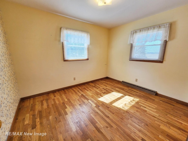 empty room with baseboards, a baseboard heating unit, and light wood-style floors