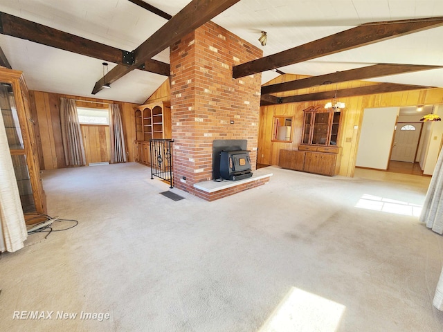 unfurnished living room featuring carpet flooring, wood walls, vaulted ceiling with beams, and a wood stove