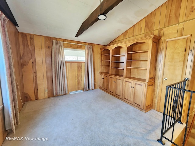 empty room with wood walls, vaulted ceiling with beams, and light colored carpet