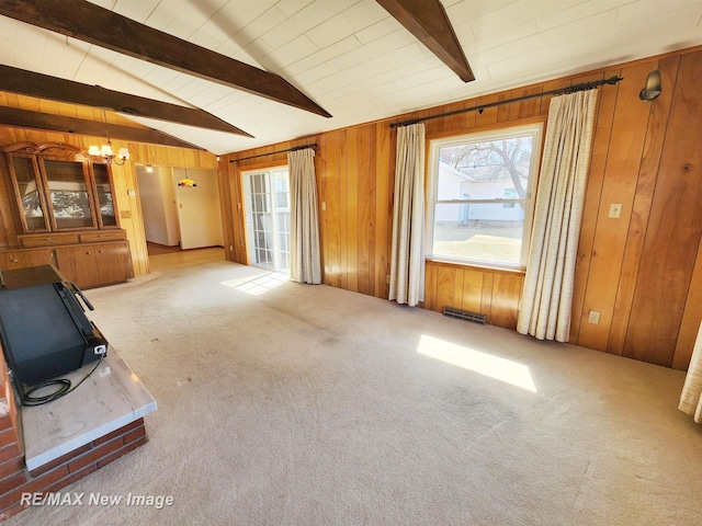 unfurnished living room featuring an inviting chandelier, wooden walls, vaulted ceiling with beams, and carpet floors