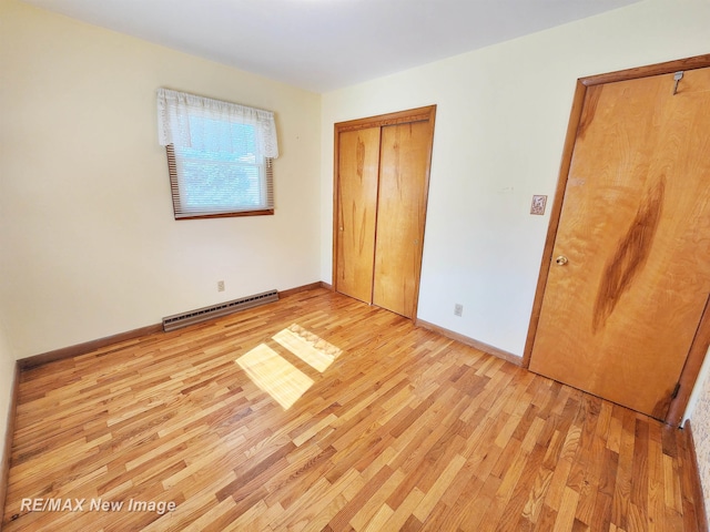 unfurnished bedroom featuring light wood-type flooring, a baseboard heating unit, baseboards, and a closet