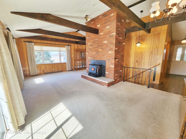 unfurnished living room featuring a wood stove, plenty of natural light, carpet, and wood walls