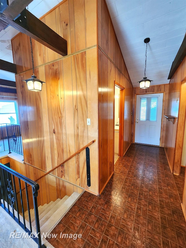 hall with brick patterned floor, vaulted ceiling, stairs, and wood walls