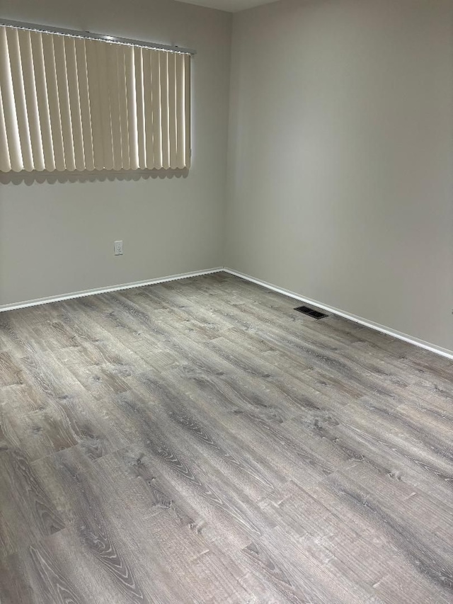 spare room with wood finished floors, visible vents, and baseboards