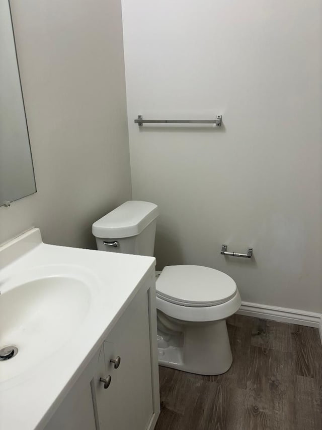 half bathroom with toilet, vanity, baseboards, and wood finished floors