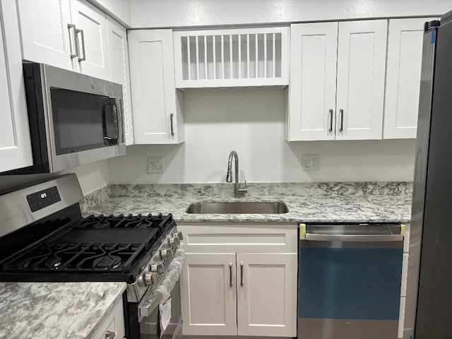 kitchen featuring light stone counters, white cabinets, appliances with stainless steel finishes, and a sink