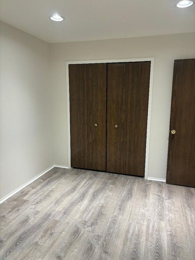 unfurnished bedroom with recessed lighting, wood finished floors, baseboards, and a closet