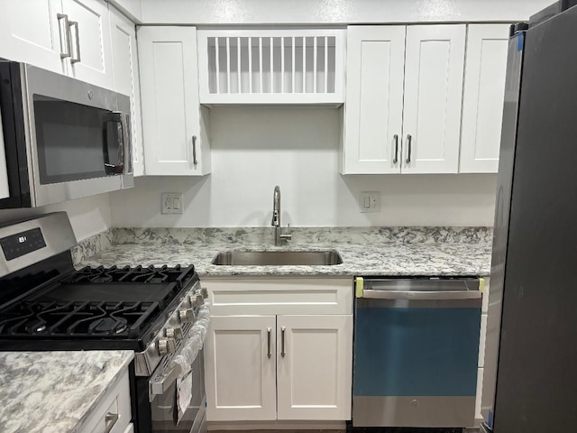 kitchen featuring light stone counters, white cabinets, stainless steel appliances, and a sink