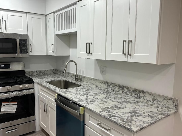 kitchen with light stone counters, white cabinets, stainless steel appliances, and a sink