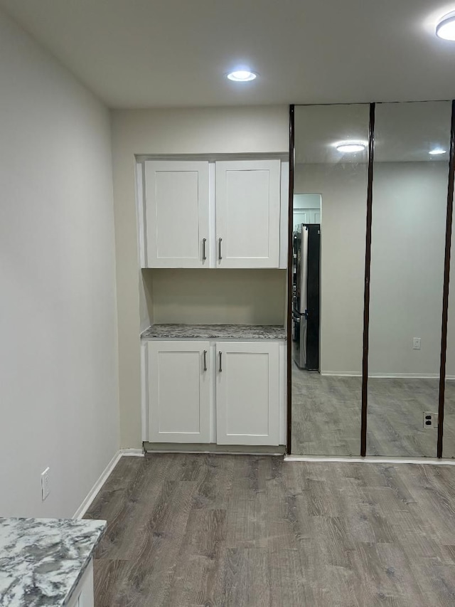 kitchen with white cabinets, freestanding refrigerator, dark wood-type flooring, and light stone countertops