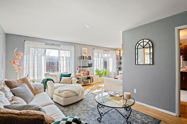 living area with an inviting chandelier, baseboards, a healthy amount of sunlight, and light wood finished floors