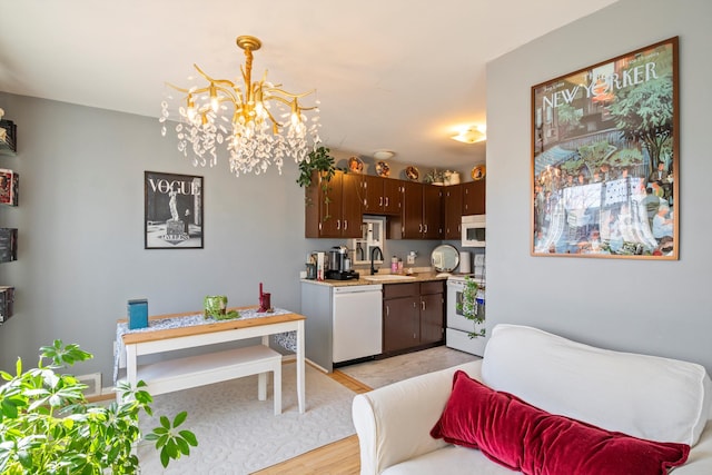 kitchen with dark brown cabinetry, light countertops, an inviting chandelier, white appliances, and a sink