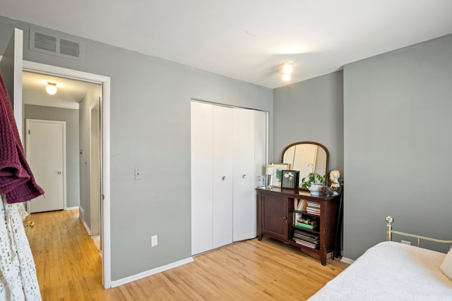 bedroom with light wood-type flooring, visible vents, baseboards, and a closet