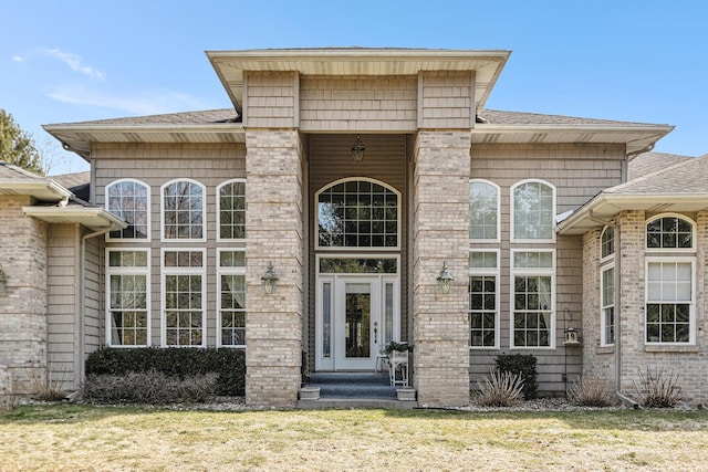 entrance to property featuring a lawn and a shingled roof