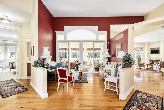 living room with light wood finished floors, visible vents, baseboards, a towering ceiling, and a glass covered fireplace