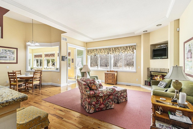 living room with a glass covered fireplace, visible vents, baseboards, and wood finished floors