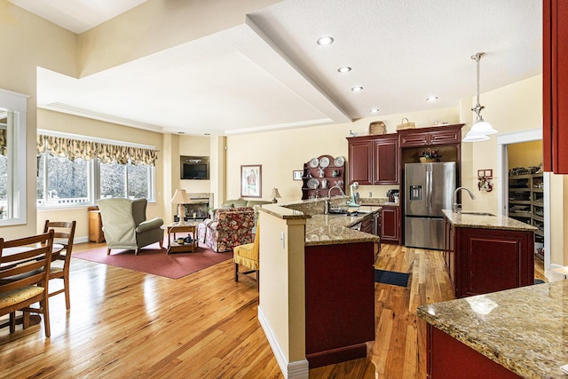 kitchen with open floor plan, stainless steel fridge, light wood-style floors, reddish brown cabinets, and a fireplace