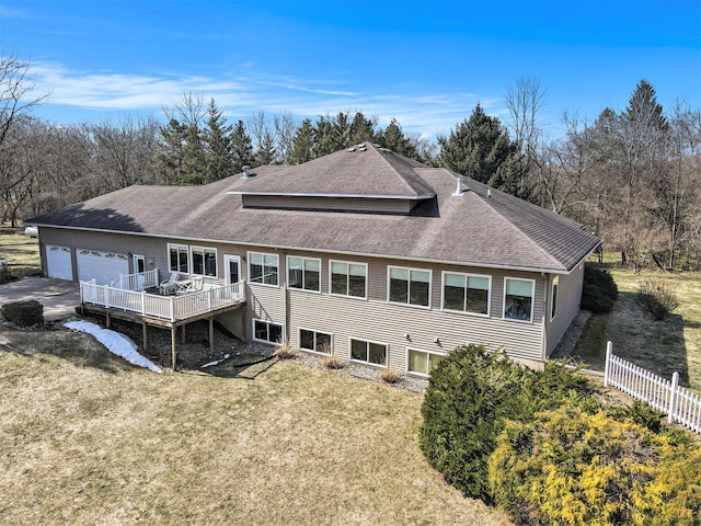 rear view of house with fence, a yard, a shingled roof, a garage, and a deck