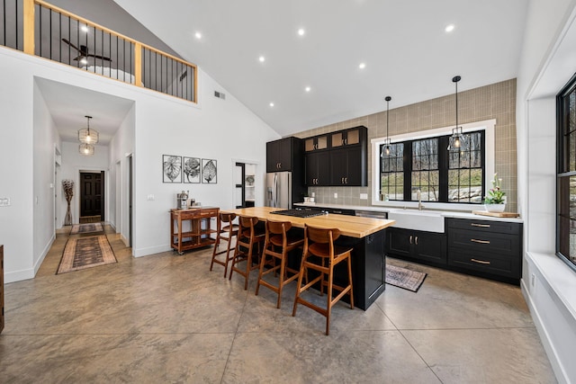 kitchen featuring a center island, concrete floors, dark cabinetry, stainless steel fridge, and a sink