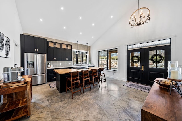 kitchen with a kitchen island, finished concrete floors, dark cabinetry, stainless steel refrigerator with ice dispenser, and high vaulted ceiling