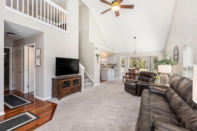 carpeted living area with stairway, ceiling fan with notable chandelier, baseboards, and a towering ceiling