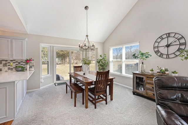 dining room with high vaulted ceiling, light colored carpet, baseboards, and a chandelier