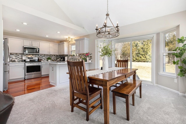 dining room with light colored carpet, lofted ceiling, a notable chandelier, and plenty of natural light