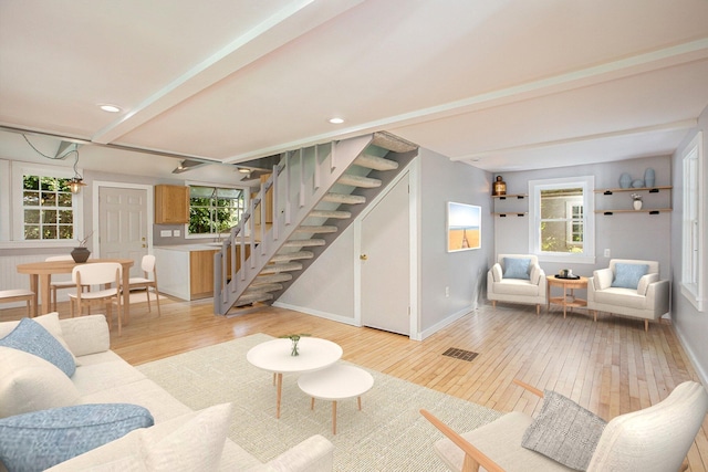 living area with stairs, light wood-style floors, and a healthy amount of sunlight