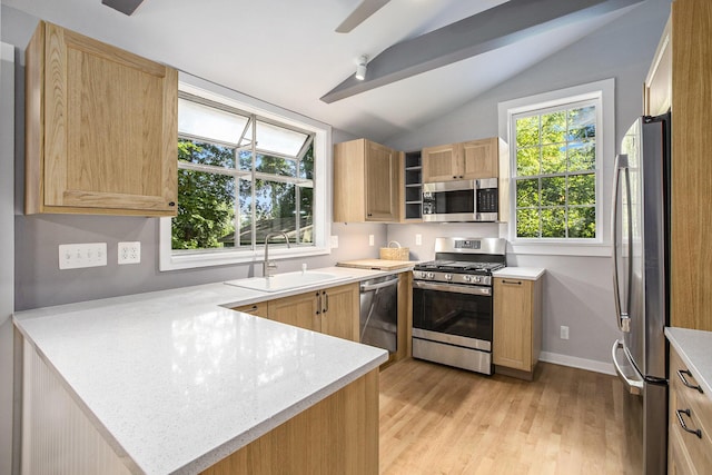 kitchen featuring light brown cabinets, a peninsula, a sink, stainless steel appliances, and vaulted ceiling