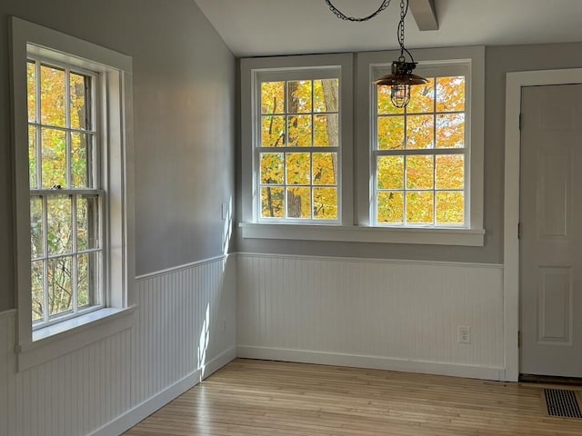 unfurnished dining area with a wainscoted wall, visible vents, and light wood-style flooring