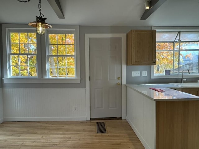 kitchen featuring visible vents, a sink, wainscoting, light wood finished floors, and light countertops