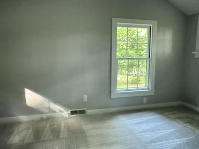 carpeted empty room with visible vents, baseboards, and vaulted ceiling