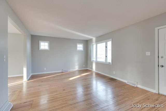 empty room with light wood finished floors, visible vents, baseboards, and a wealth of natural light