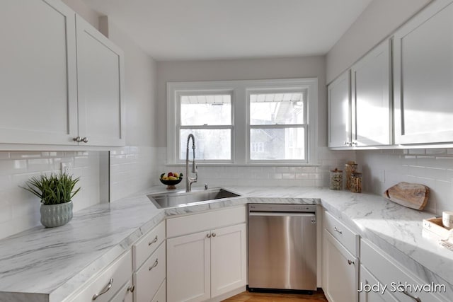 kitchen featuring stainless steel dishwasher, white cabinets, backsplash, and a sink