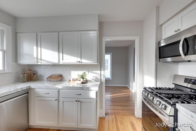 kitchen featuring light wood-style flooring, tasteful backsplash, appliances with stainless steel finishes, white cabinets, and light stone countertops