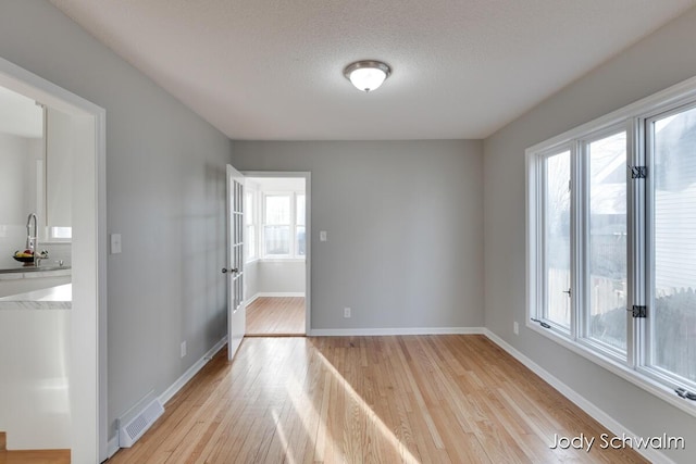 empty room with light wood-type flooring, visible vents, a sink, a textured ceiling, and baseboards