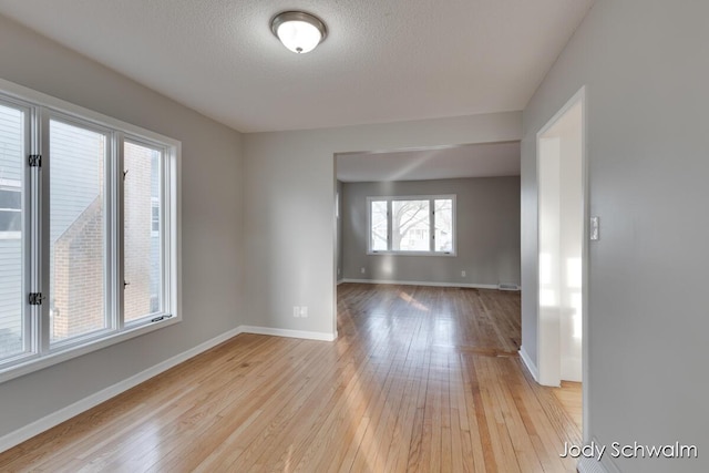 empty room with light wood finished floors, a textured ceiling, and baseboards