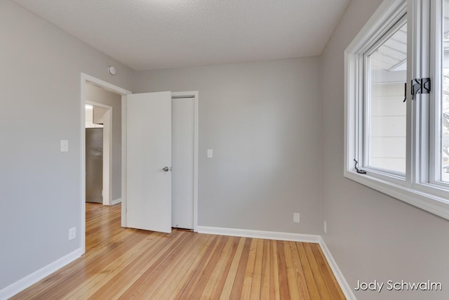 unfurnished room featuring a textured ceiling, light wood-type flooring, and baseboards