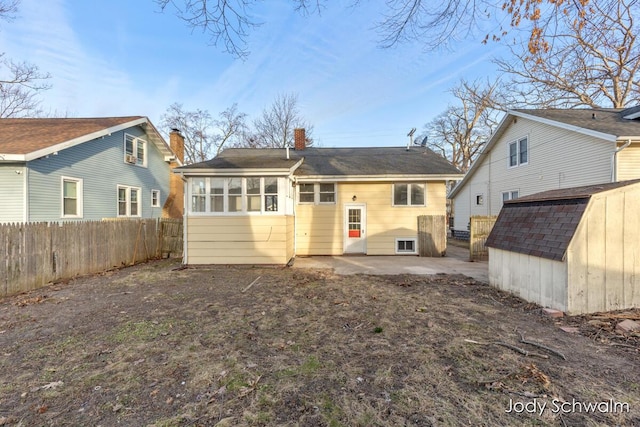 back of property featuring fence, a chimney, an outdoor structure, a storage shed, and a patio area