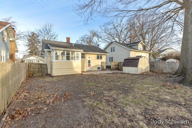 back of property with a shed, a chimney, a fenced backyard, an outbuilding, and a patio