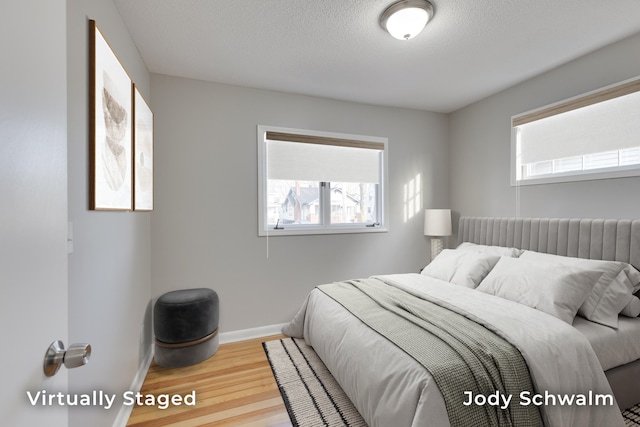 bedroom featuring multiple windows, a textured ceiling, baseboards, and wood finished floors