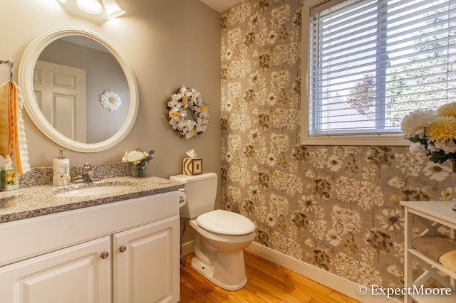 bathroom featuring vanity, wood finished floors, baseboards, wallpapered walls, and toilet